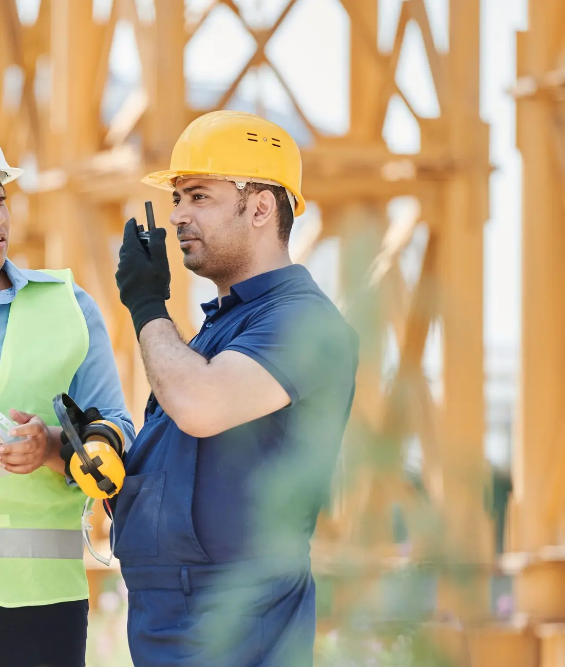 Ingeniera e ingeniero de obra conversando con planos y radio