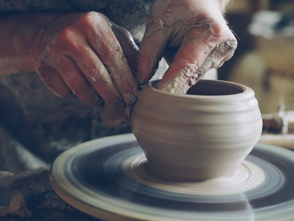 Manos modelando una taza de barro en el torno