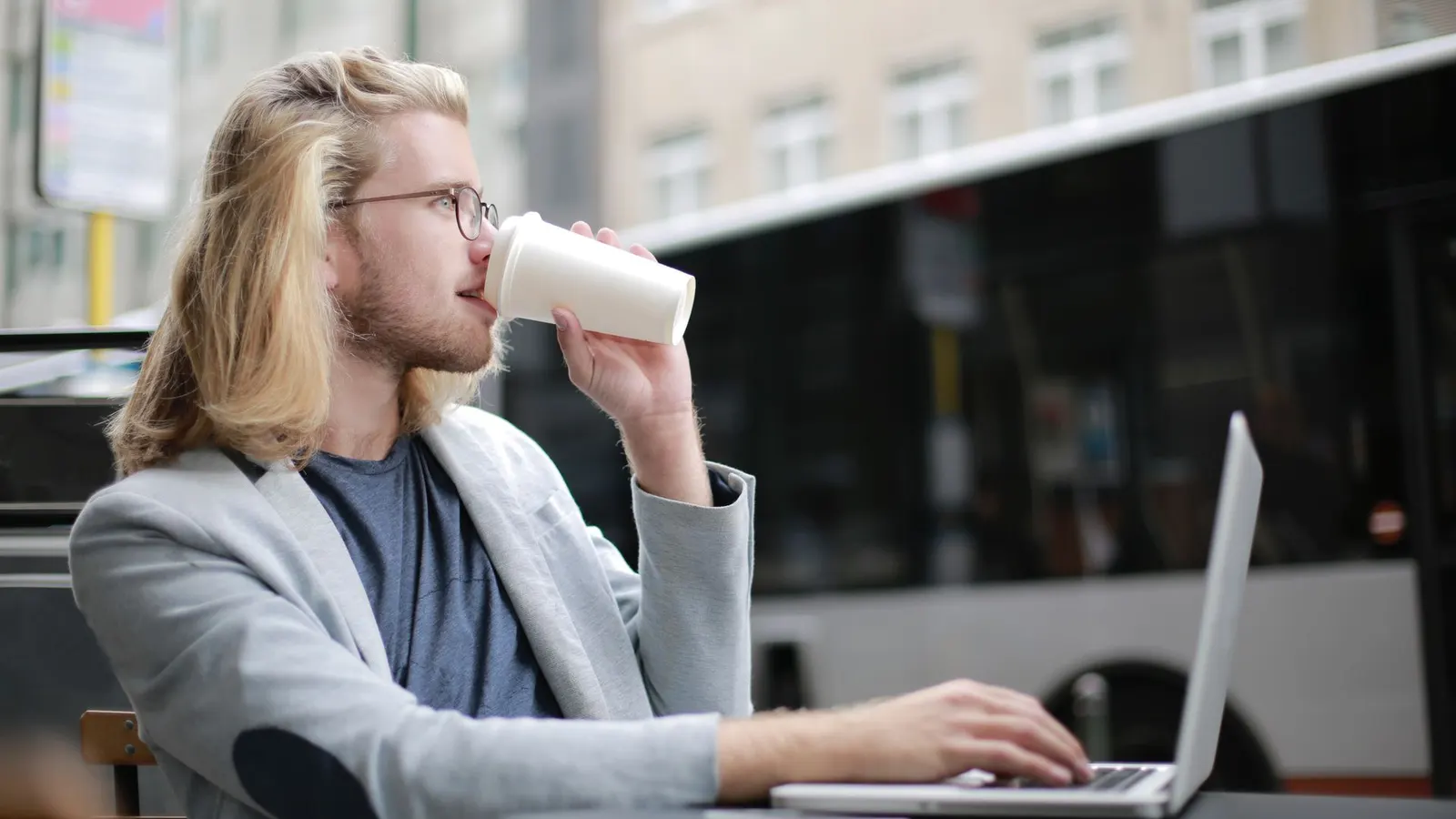 Joven trabajando de forma remota con su laptop y un café al aire libre