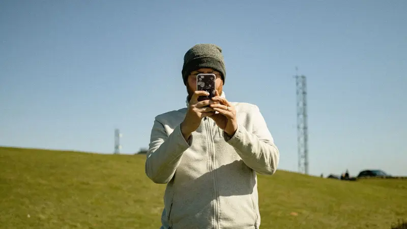 Hombre con gorro usando su celular al aire libre en una zona rural