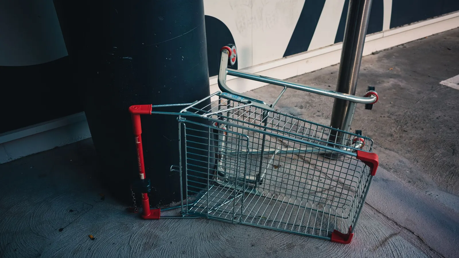 Carrito de supermercado volcado en el suelo, abandonado junto a una pared
