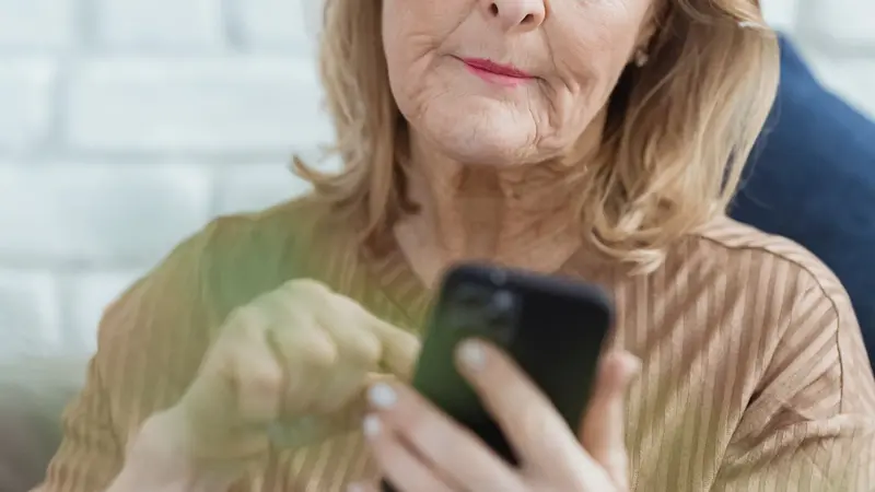 Persona adulta mayor usando su celular sentada en su casa