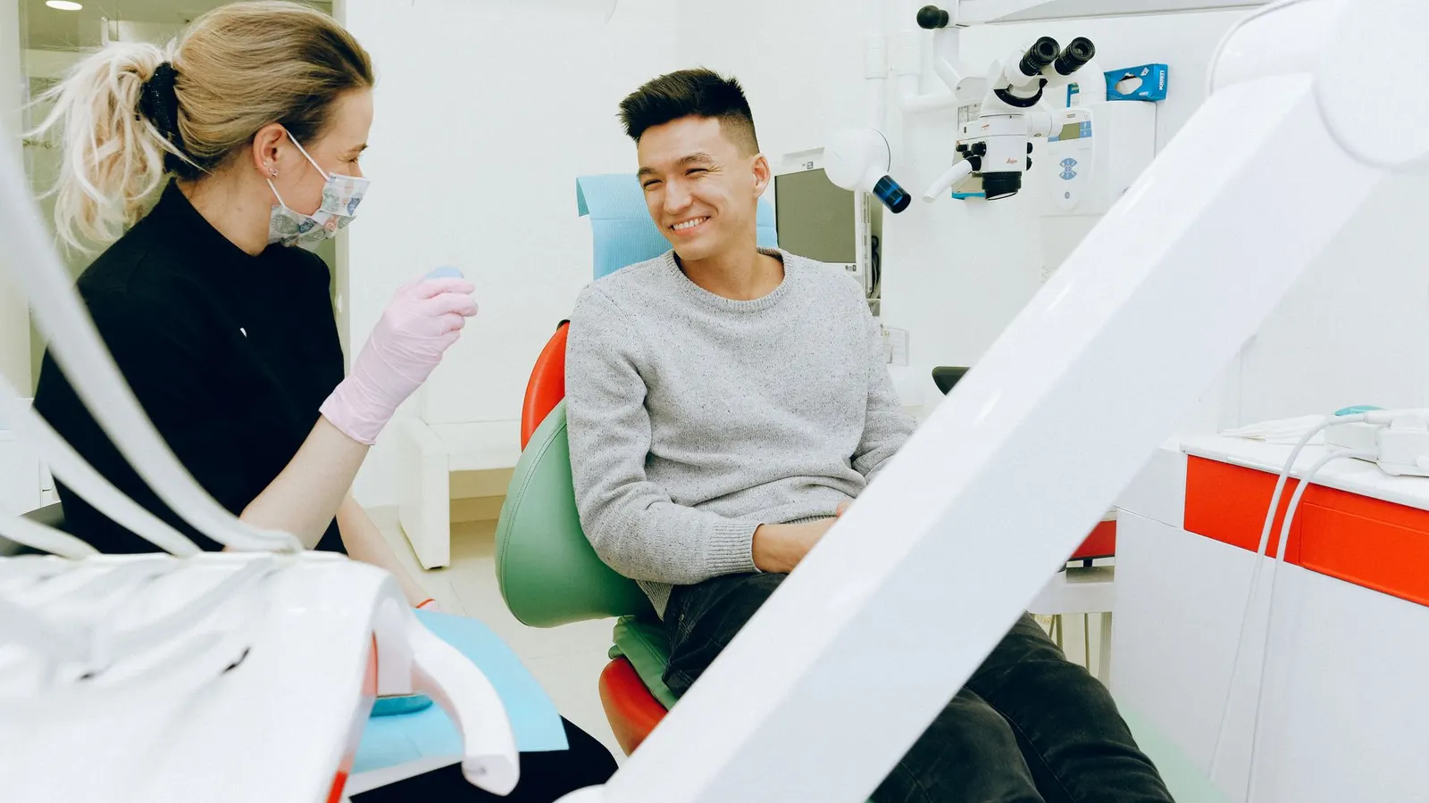 Una odontóloga con barbijo y guantes conversa con un paciente sonriente sentado en el sillón dental