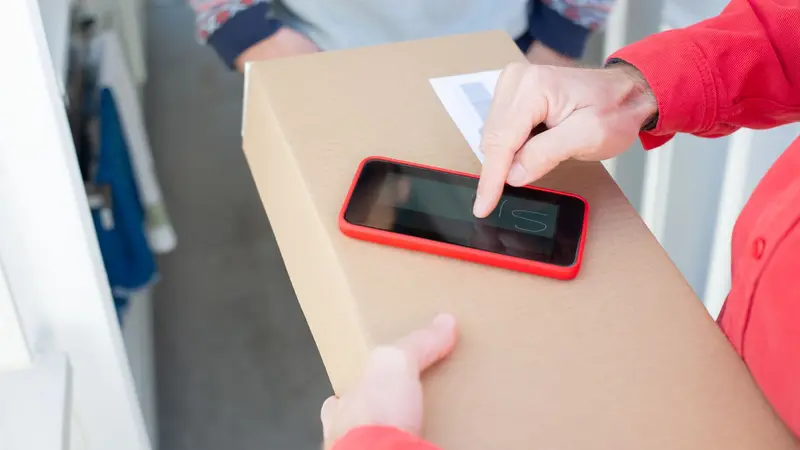 Persona empacando un producto para envío junto a una laptop abierta con una tienda online, en un pequeño local comercial