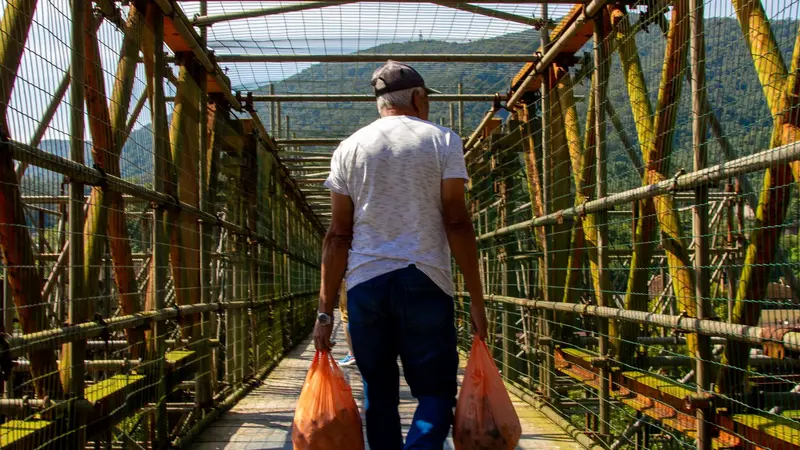 Hombre caminando por un puente cargando bolsas de compras