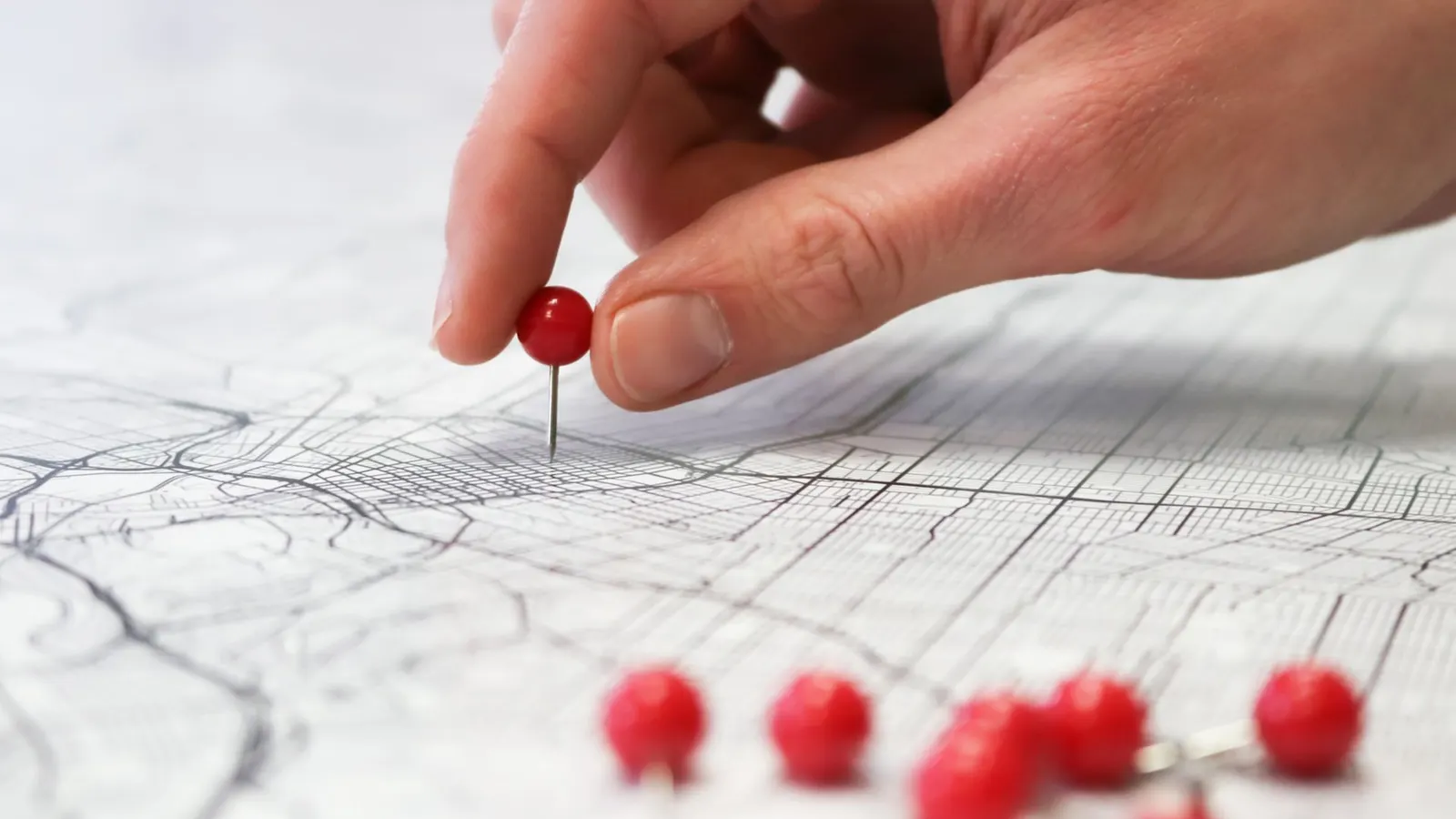 Uma mão espeta um alfinete vermelho num mapa de ruas impresso