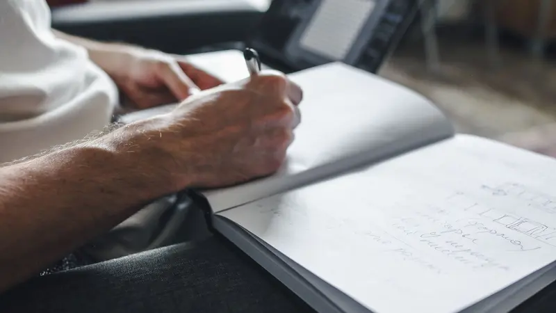 Persona enfocada escribiendo notas junto a una laptop