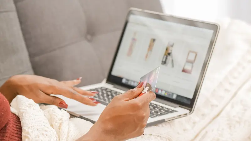 Manos con una tarjeta frente a una laptop con una tienda online abierta, sobre un sillón