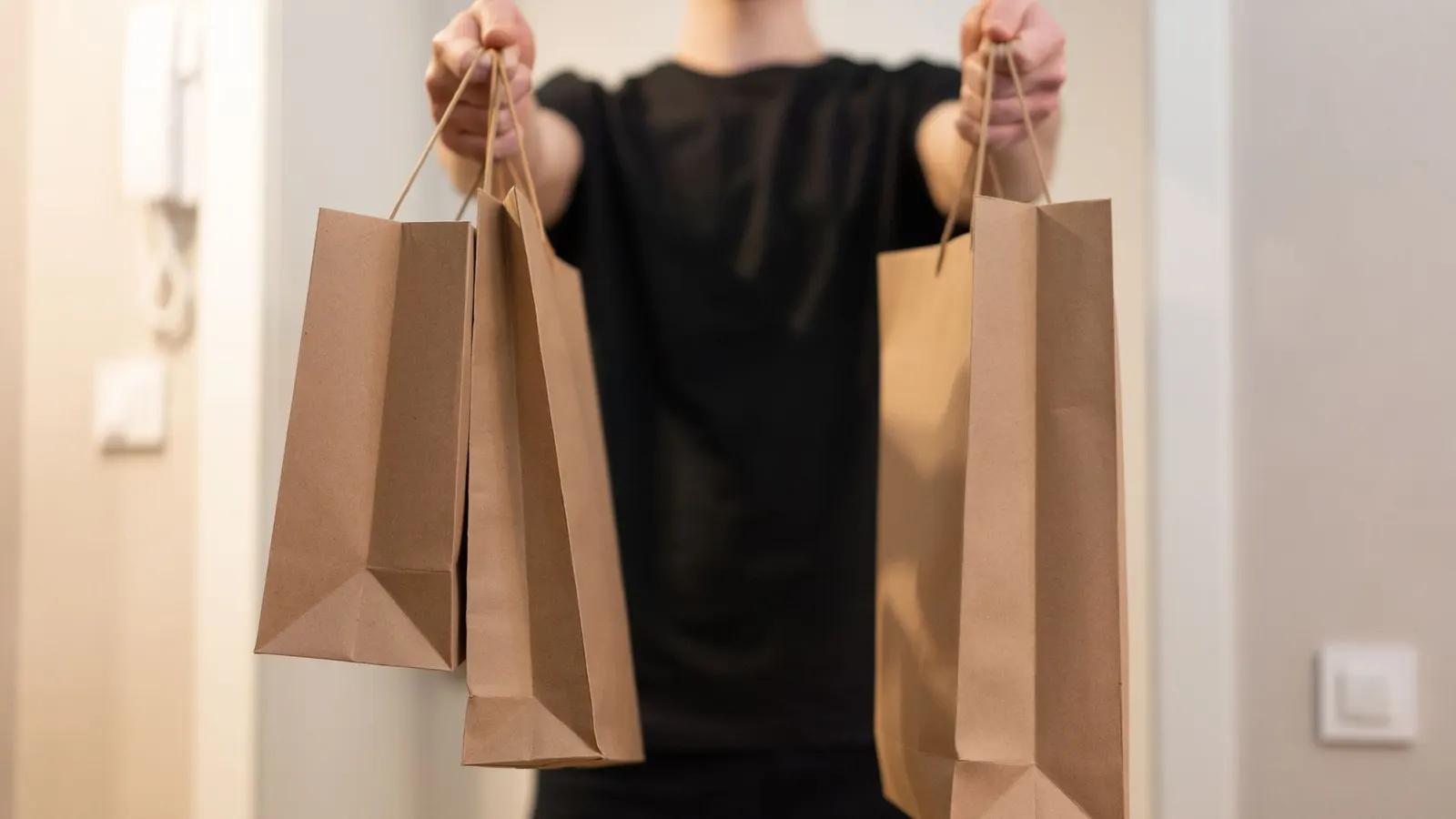 Una persona de remera negra extiende los brazos para entregar tres bolsas de papel madera con un pedido
