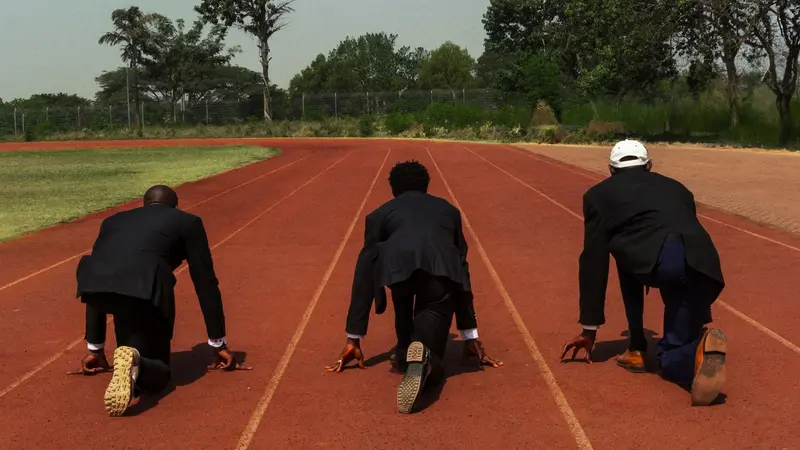 Empresarios agachados en la línea de largada de una pista de atletismo