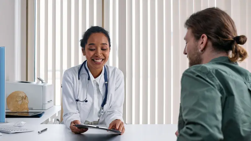 Médica conversando de forma positiva com um paciente em um consultório iluminado