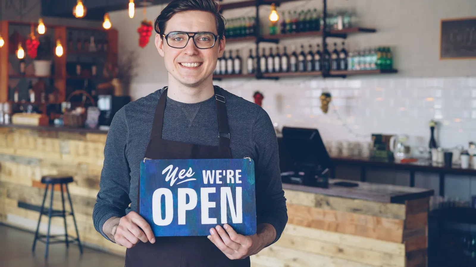 Dueño de un local sonriendo mientras sostiene un cartel que dice que el negocio está abierto