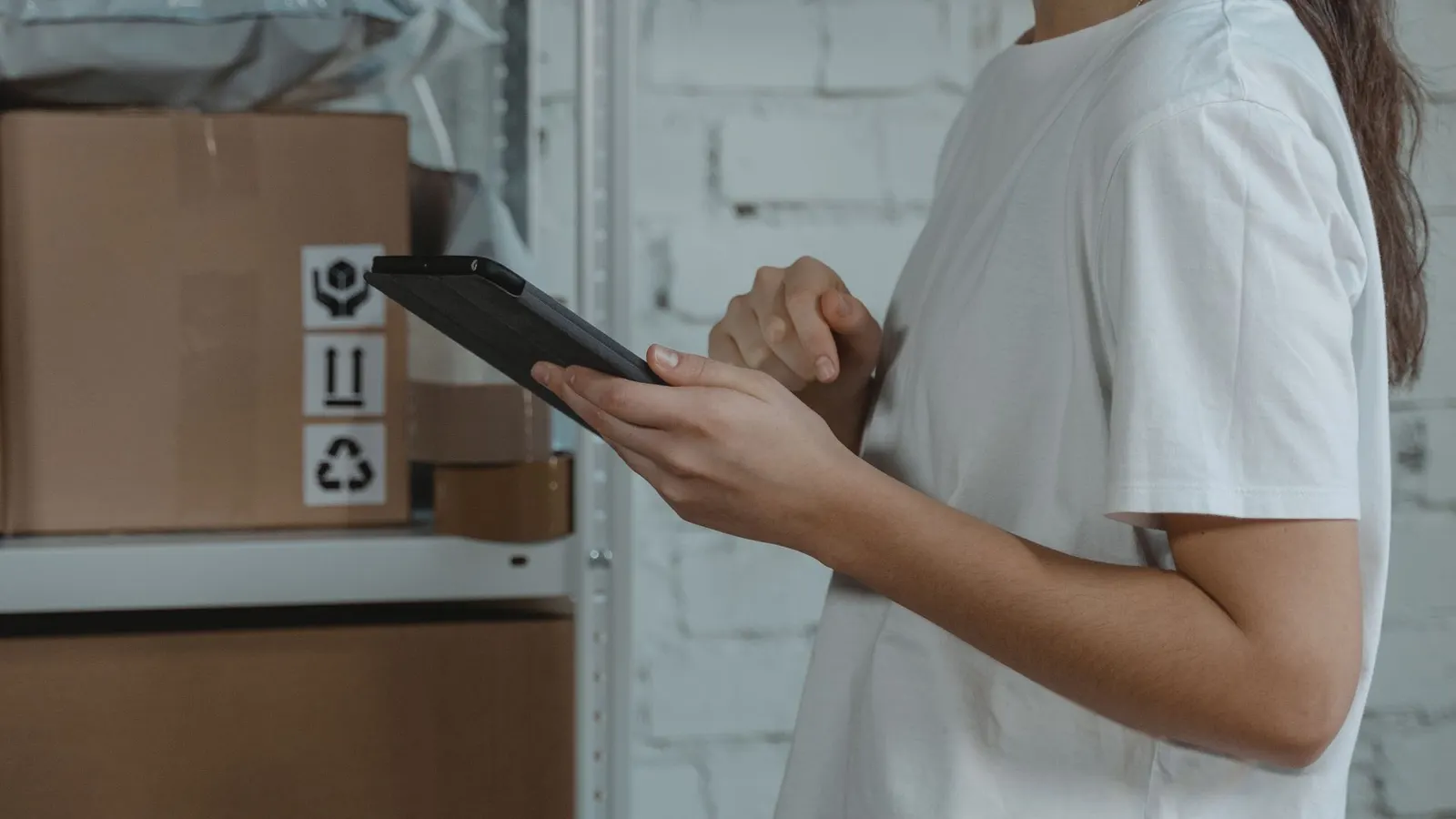 Persona registrando pedidos en una tablet junto a cajas listas para despacho