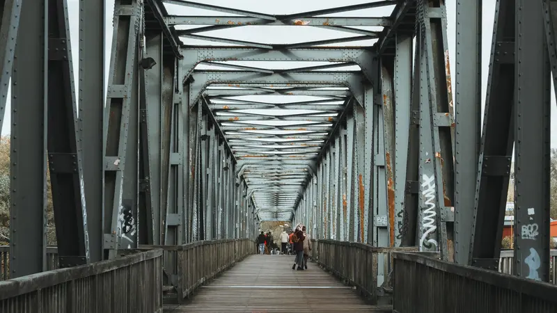 Puente peatonal moderno visto desde abajo con gente cruzando al atardecer