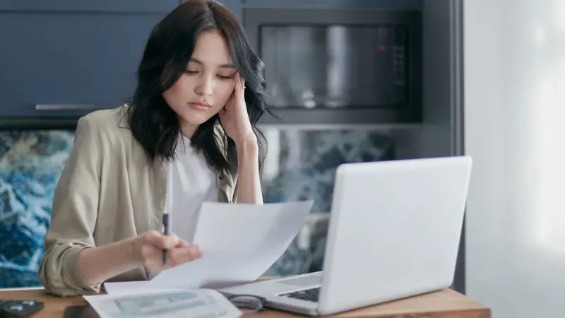 Mujer revisando un presupuesto impreso frente a su computadora portátil