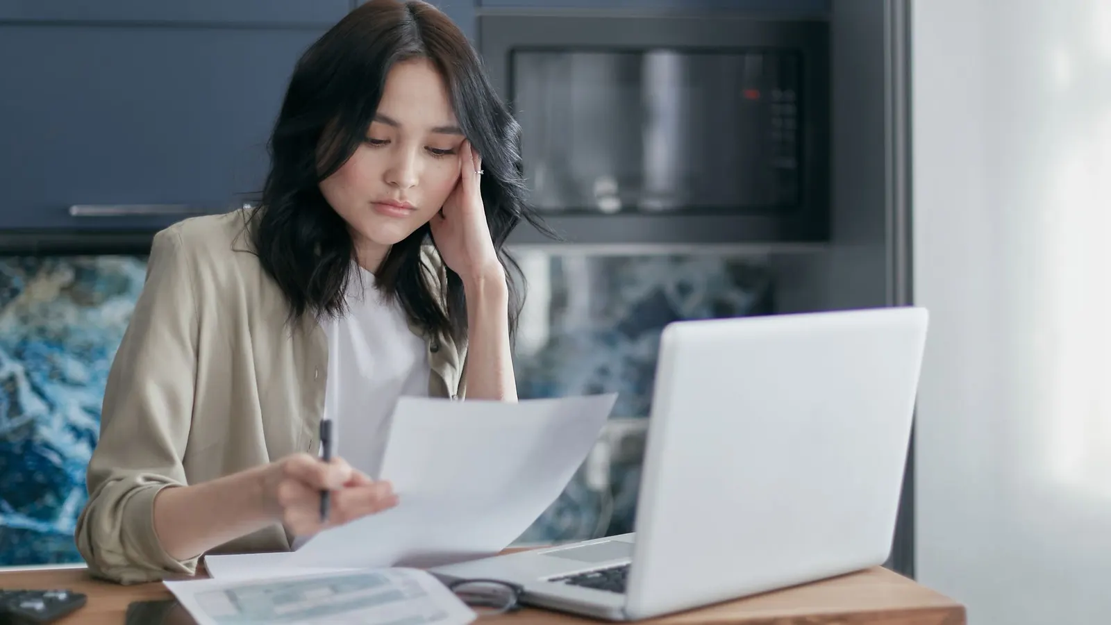 Mujer revisando un presupuesto impreso frente a su computadora portátil