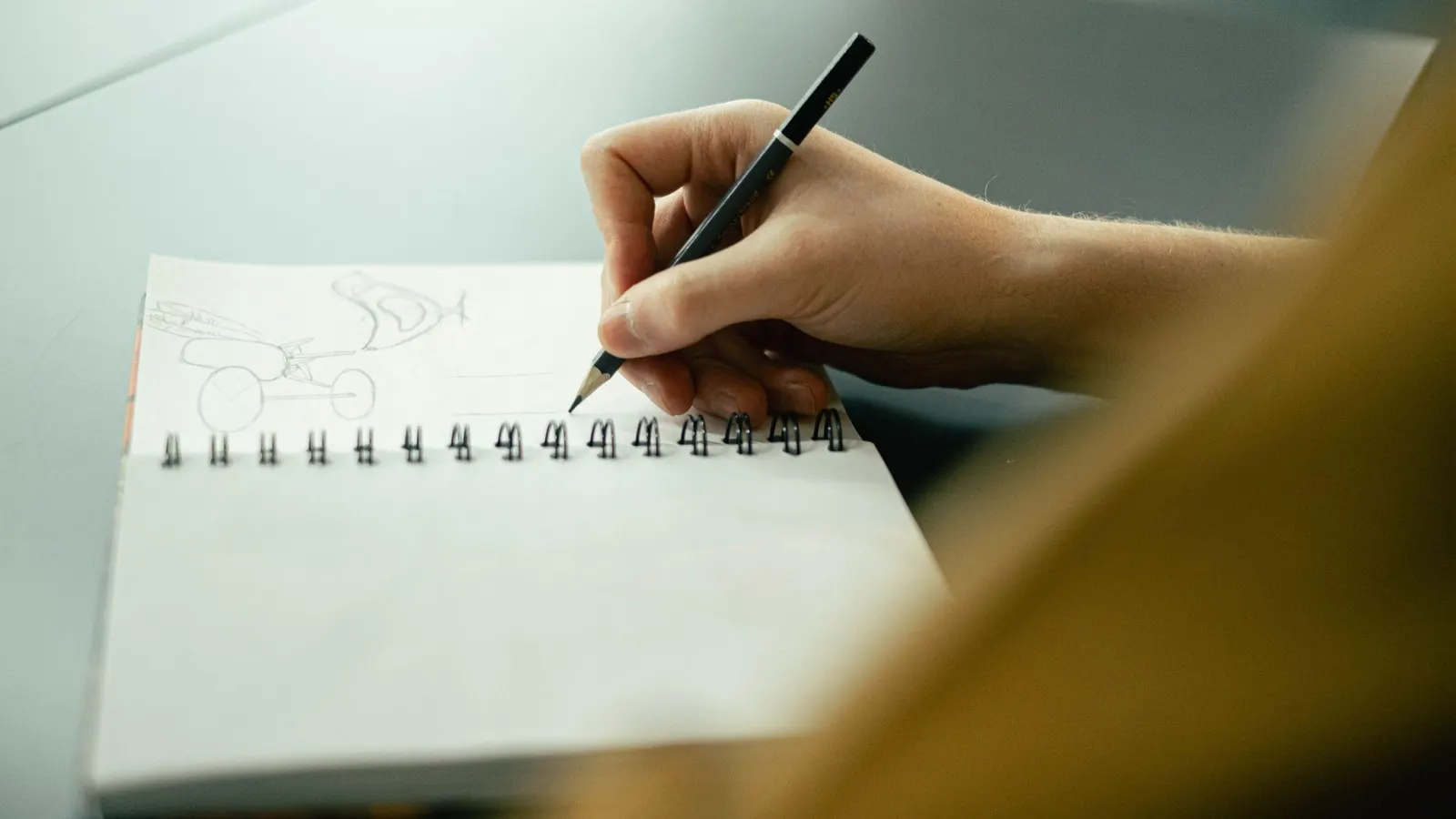 Uma mão desenha a lápis os primeiros esboços num caderno de espiral
